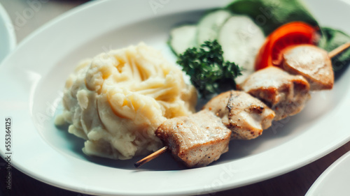 kebab on a wooden skewer with mashed potatoes and fresh vegetables