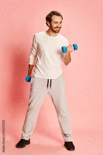 Active happy man with beard wearing home sportswear doing exercises isolated over pink background. Concept of active lifestyle, positive emotions, sport © Lustre Art Group 