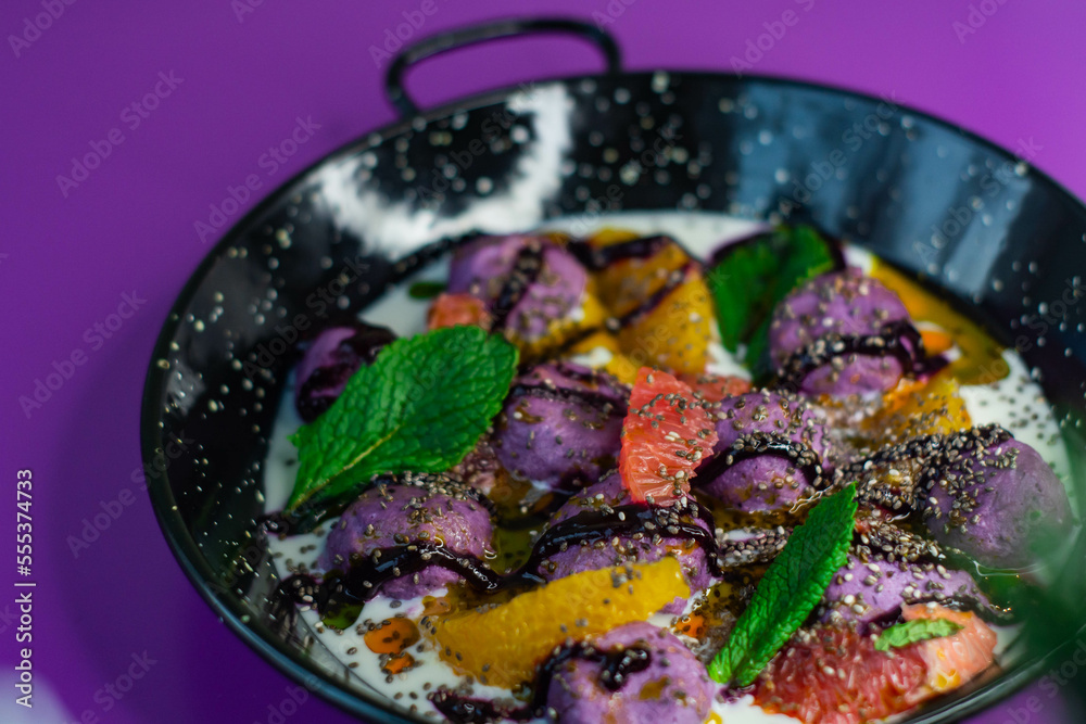 Breakfast in black plate on purple background with lazy cheesecakes currant, strawberry, blueberry, chia, mint and coconut sauce.