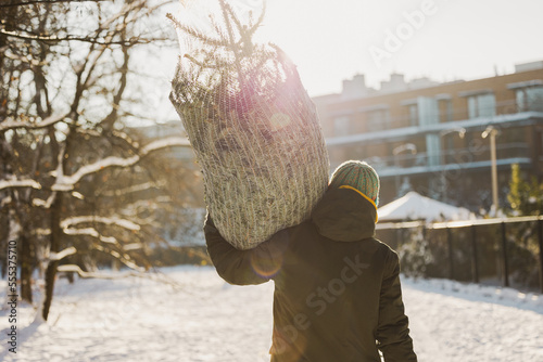 Man carrying Christmas tree on shoulders outdoors
