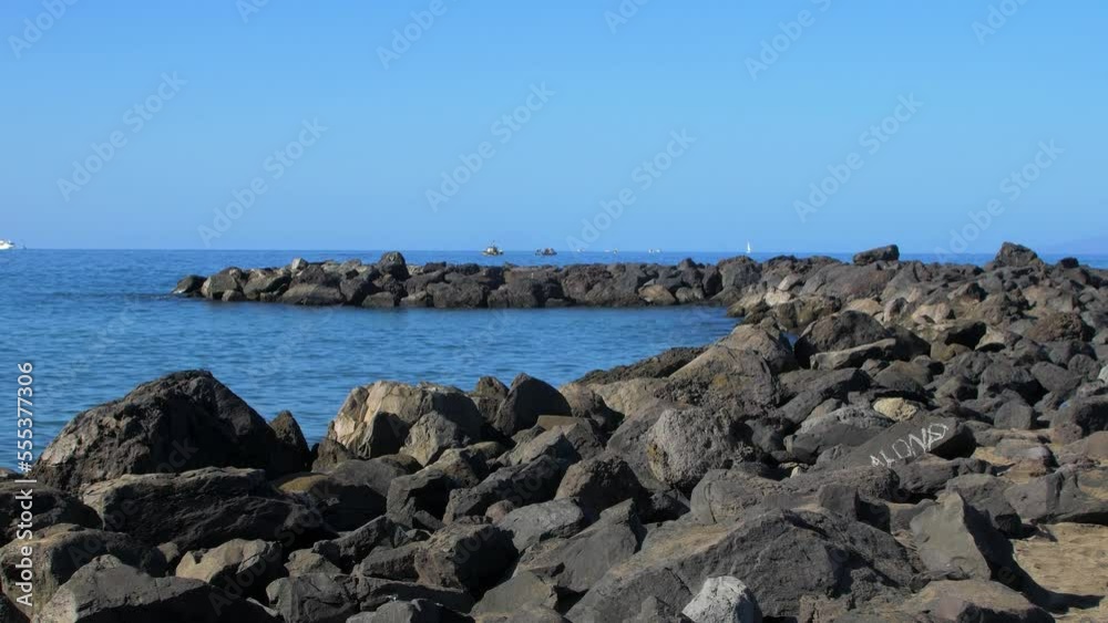 Stone pier at the beach of Playa De Las Americas (Tenerife, Spain), sunny summer day, calm Atlantic ocean in the background, medium handheld shot Stone pier at the beach of Playa De Las Americas (Tenerife, Spain), sunny summer day, calm Atlantic ocean in the background, medium handheld shot
