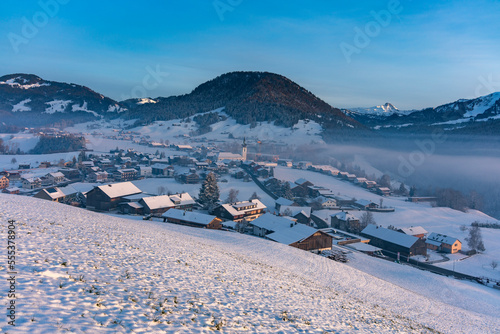 Panorama mit dem Dorf Hittisau im Bregenzerwald im ersten Schnee. Winter in Vorarlberg, mit Bergdorf, Wiesen, Wälder und Berge im Hintergrund