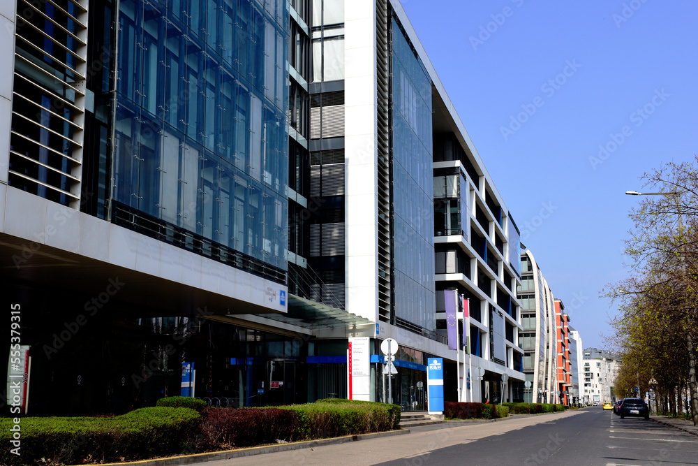 Obraz premium street in Budapest with a row of modern glass office buildings in the spring. green trees. diminishing perspective. curtain wall facades. asphalt road. business and architecture. blue sky. cityscape.