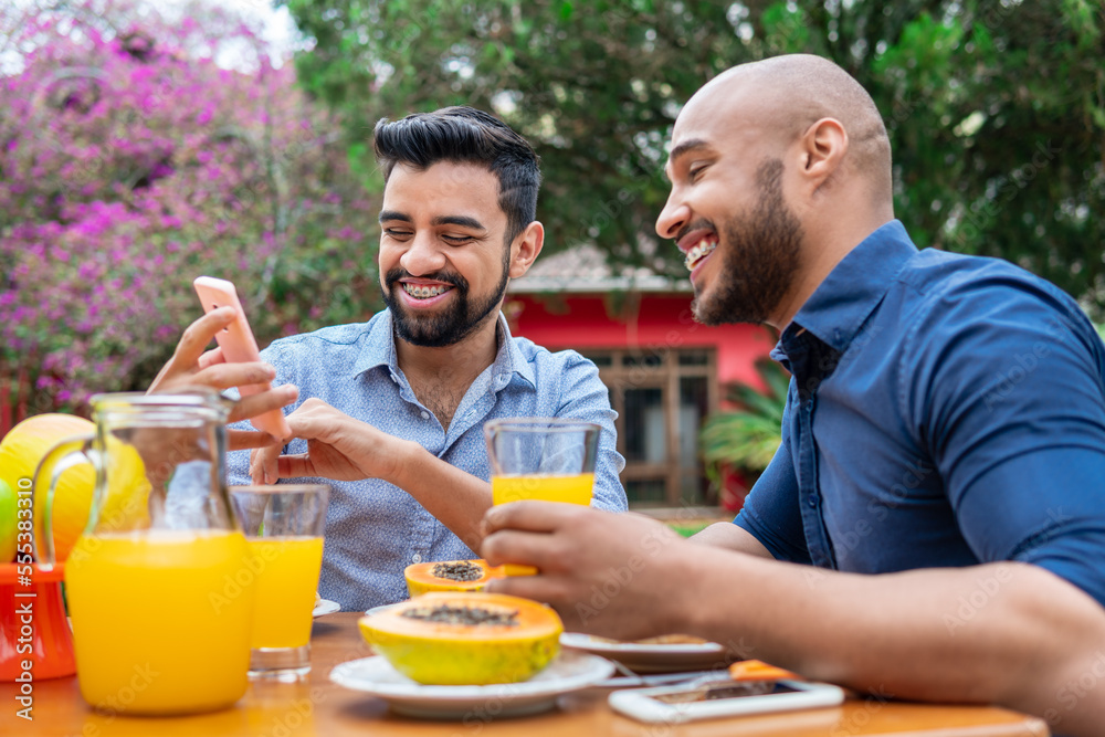 happy gay couple laughing and looking at mobile phone for fun in table outside