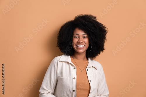 happy black young woman smiling and standing wearing white jacket in beige background. portrait, real people concept.