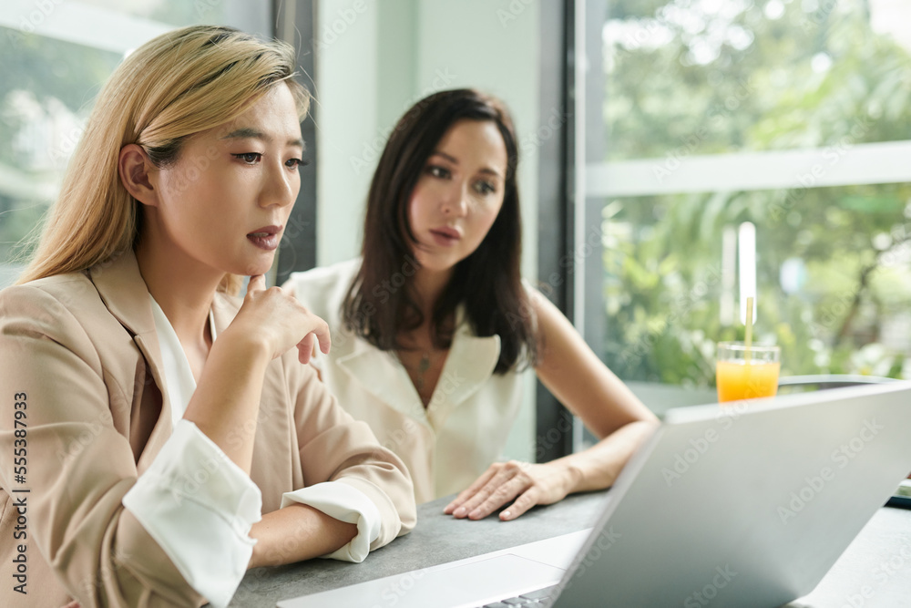 Serious businesswomen discussing report on laptop screen at meeting