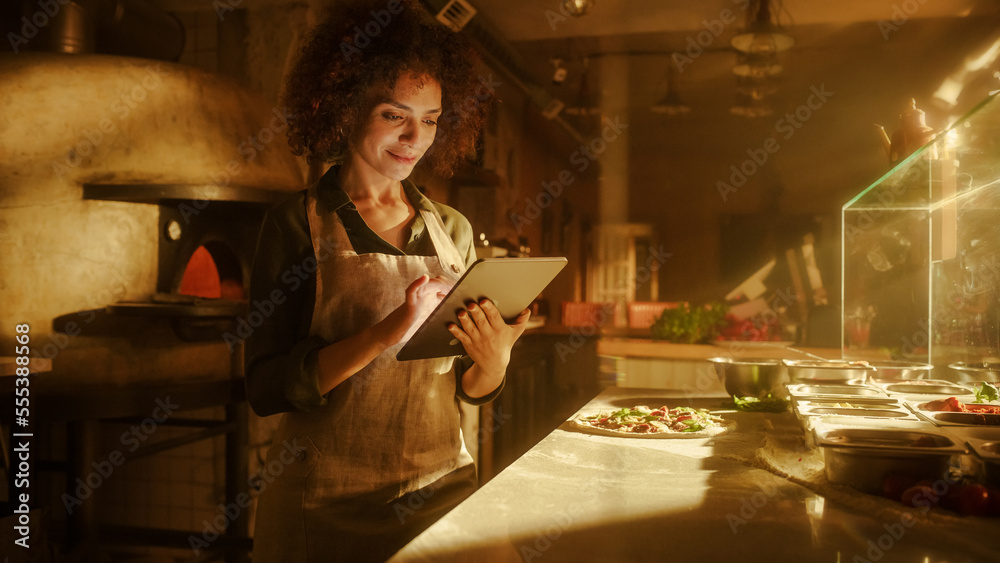 In Restaurant: Beautiful Female Chef Using Laptop Computer. Authentic Pizza Place Cooking Delicious Organic Eco Food. Bi-racial Female Entrepreneur Working on Online Order, Small Business Family Shop