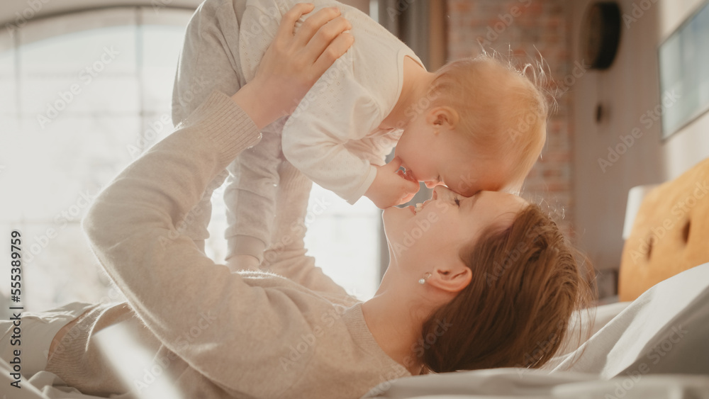 Young Caring Mother Playing and Nursing Adorable Baby at Home. Beautiful Mom and Cute Little Infant Child Cuddling in Bedroom. Motherhood Tender Moments. Young Caring Mother Playing and Nursing Adorable Baby at Home. Beautiful Mom and Cute Little Infant Child Cuddling in Bedroom. Motherhood Tender Moments.