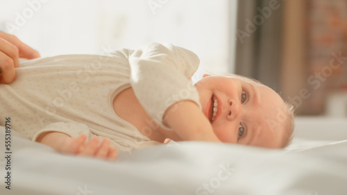 Beautiful Baby Portrait: Adorable Infant Sitting in Bed and Looking at Camera. Happy Child with Light Blond Hair at Home. Concept of Childhood, New Life, Motherhood.