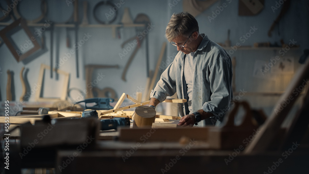 Portrait of an Artisan Furniture Designer Reading Blueprint and Starting to Assemble Legs of a Wooden Chair. Stylish Carpenter Working in a Studio in Loft Space with Tools on the Walls.