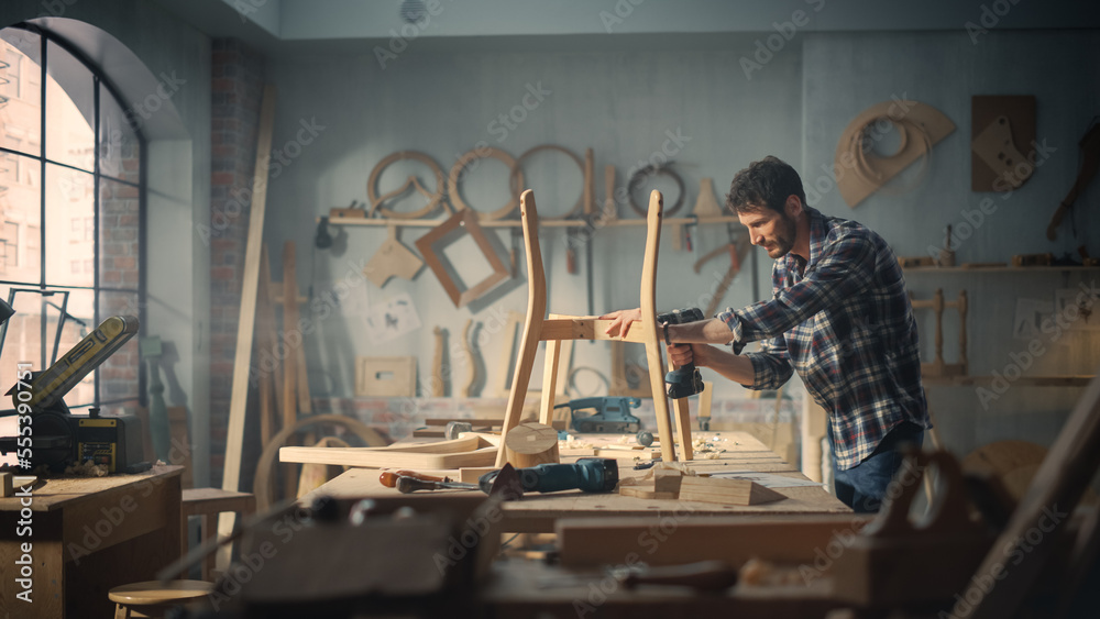 Young Carpenter Reading Blueprints and Starting to Assemble Parts of a Wooden Chair with a Rubber Hammer. Stylish Furniture Designer Working in a Studio in Loft Space with Tools on the Walls.