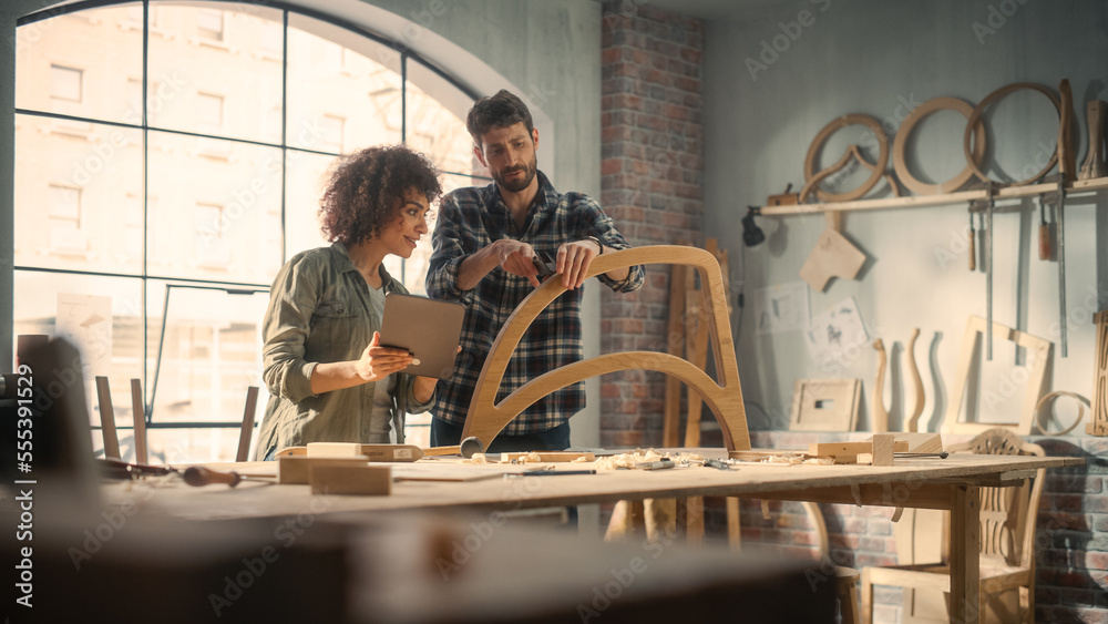 Excited Young Man and Woman Using Tablet Computer, Discussing a Successful Project in a Carpentry Studio. Furniture Designers Working in Loft Studio. Excited Young Man and Woman Using Tablet Computer, Discussing a Successful Project in a Carpentry Studio. Furniture Designers Working in Loft Studio.