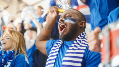 Sport Stadium Big Event: Handsome Black Man Cheering. Crowd of Fans with Painted Faces Cheer, Shout for their Blue Soccer Team to Win. People Celebrate Scoring a Goal, Championship Victory.