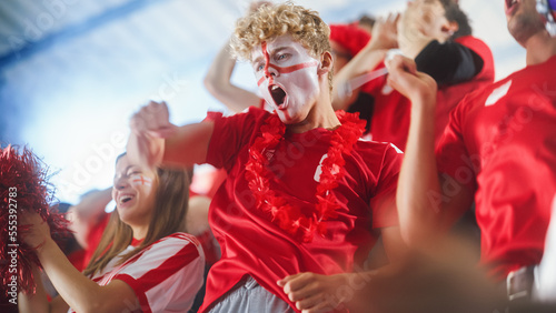 Sport Stadium Big Event: Handsome Emotional Man Cheering. Crowd of Fans with Painted Faces Shout for Red Soccer Team to Win. People Celebrate Scoring a Goal, Championship Victory