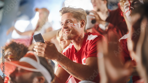 Sport Stadium Soccer Match: Caucasian Man Using Smartphone Cheering for Red Team to Win, Looking at Mobile Phone to Check App, Bet, Score, Winnings. Crowd Celebrate Goal, Championship Victory