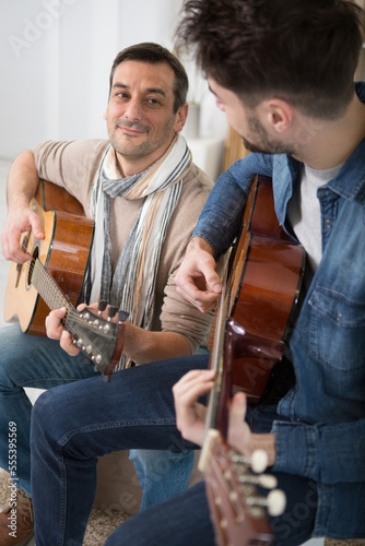 father with small son sitting on sofa indoors playing guitar photo