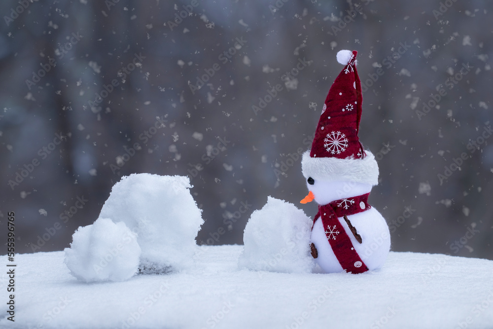 Fabulous winter background with a toy snowman.Funny toy snowman sculpts a snowman from natural snow.