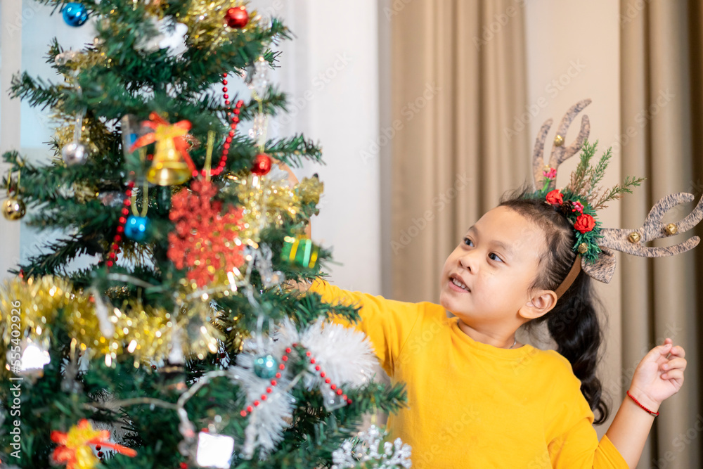 Happy Asian Baby girl decorate A Christmas tree at home, Happy New Year and Christmas Party Concept.
