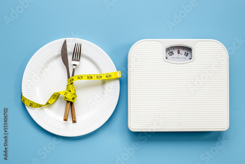 Weight scale and tape measure over dinner fork and knife on the plate
