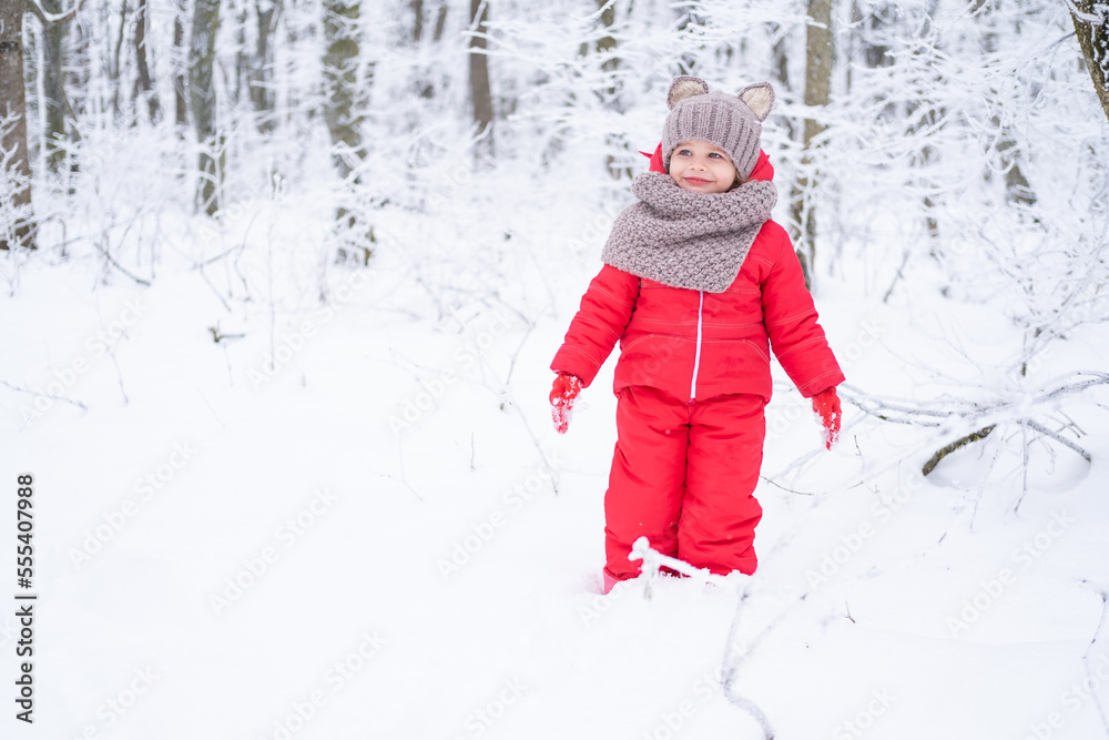 Cute little girl in pink snowsuit and knitted hat and scarf plays with snow in winter forest Cute little girl in pink snowsuit and knitted hat and scarf plays with snow in winter forest