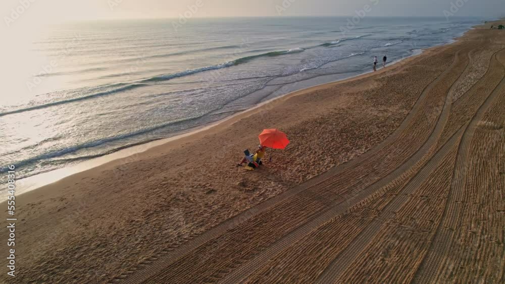 Top view aerial drone shooting young guy freelancer works on a laptop while he relaxes on the beach near the calm sea during his vacation. Hipster boy uses a laptop. Top view aerial drone shooting young guy freelancer works on a laptop while he relaxes on the beach near the calm sea during his vacation. Hipster boy uses a laptop.