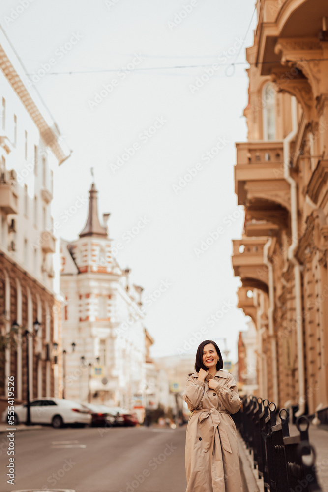 a beautiful brunette woman in a raincoat stops a car on the street of the city.
