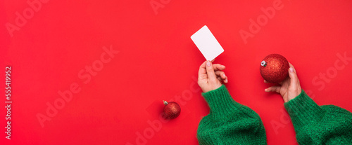 Christmas shopping concept. Flat lie hands in a green sweater with bonus card. Banner on a red background