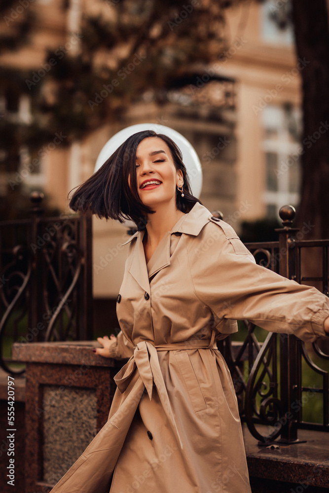 Fototapeta premium a brunette woman in a raincoat walks through the streets of the autumn city.