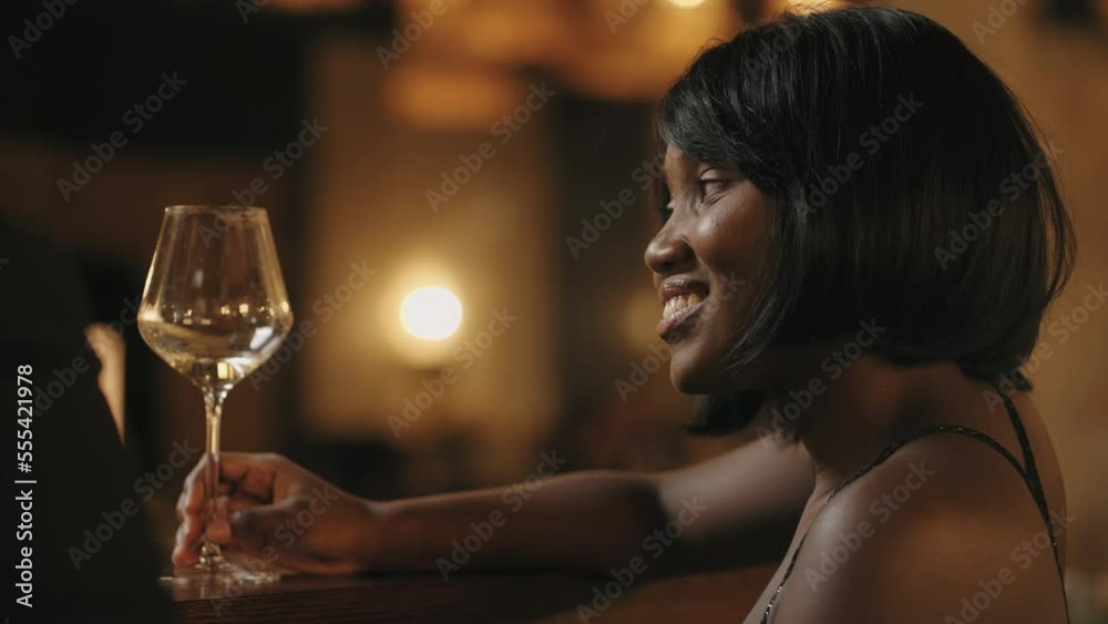 portrait of beautiful young black woman in bar, drinking wine and flirting with man