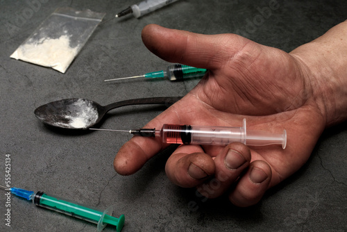 Syringe for injection in a man's hand. The hand holds the syringe. The concept of drug addiction, possession and distribution.