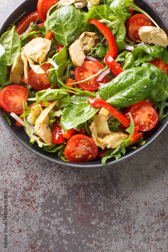 Dietary salad of pickled artichokes, tomatoes, spinach, arugula, fried peppers and onions close-up in a plate on the table. Vertical top view from above Dietary salad of pickled artichokes, tomatoes, spinach, arugula, fried peppers and onions close-up in a plate on the table. Vertical top view from above