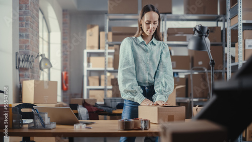 Small Business Owner Packaging a Stylish Yellow Coat Seat Sold to a Client Online. Preparing a Small Cardboard Box for Postage. Beautiful Female Inventory Manager Working in Warehouse Facility.
