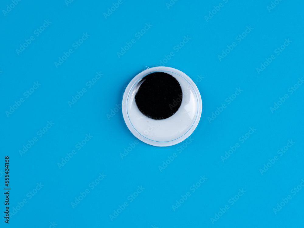 single wobbly googly eye isolated on a light blue  background with copyspace business logo - obrazy, fototapety, plakaty 
