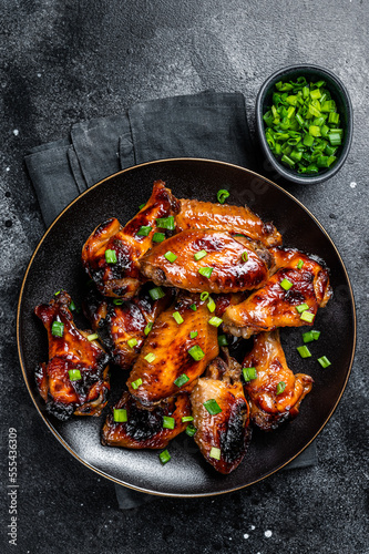 Baked chicken wings with sweet chili sauce in a plate. Black background. Top view