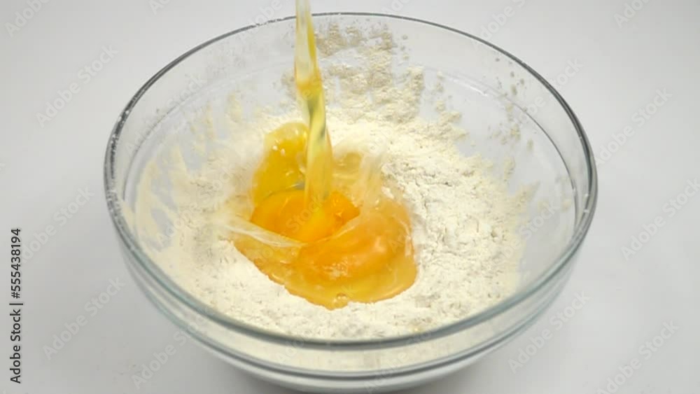 A raw chicken egg falls slowly into a glass bowl of flour, slow motion A raw chicken egg falls slowly into a glass bowl of flour, slow motion