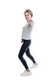 A young woman jumps happily. A beautiful blonde woman wearing a t-shirt, black jeans and white sneakers. Energy, activity and positive. Isolated on white background. Vertical. Side view.
