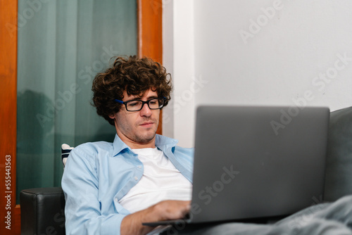 Businessman lying on the couch doing remote freelance job, working on internet at home with laptop computer