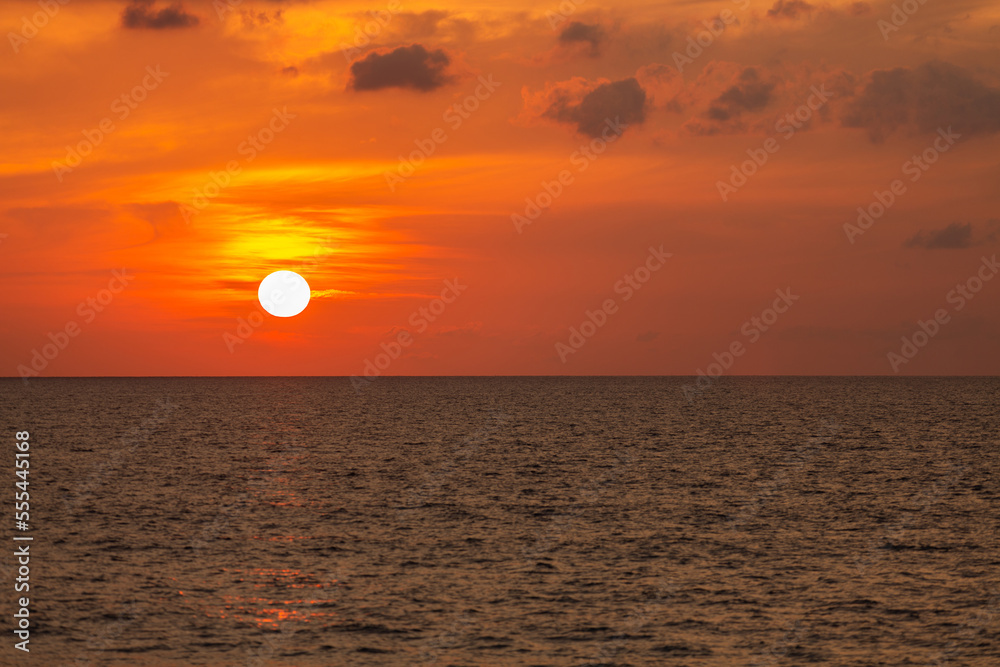 Image of a large sun on the beach with waves crashing Shining through the clouds, the golden sky looks so relaxing.