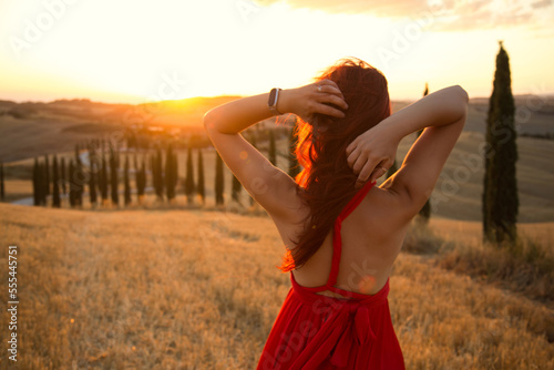 A girl at sunset in a red dress on a field in Italian Tuscany. Val d'Orcia. Beautiful landscape scenery at sunset of Tuscany in Italy