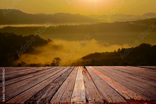 An empty wooden terrace with mountain view and mist during sunrise.	