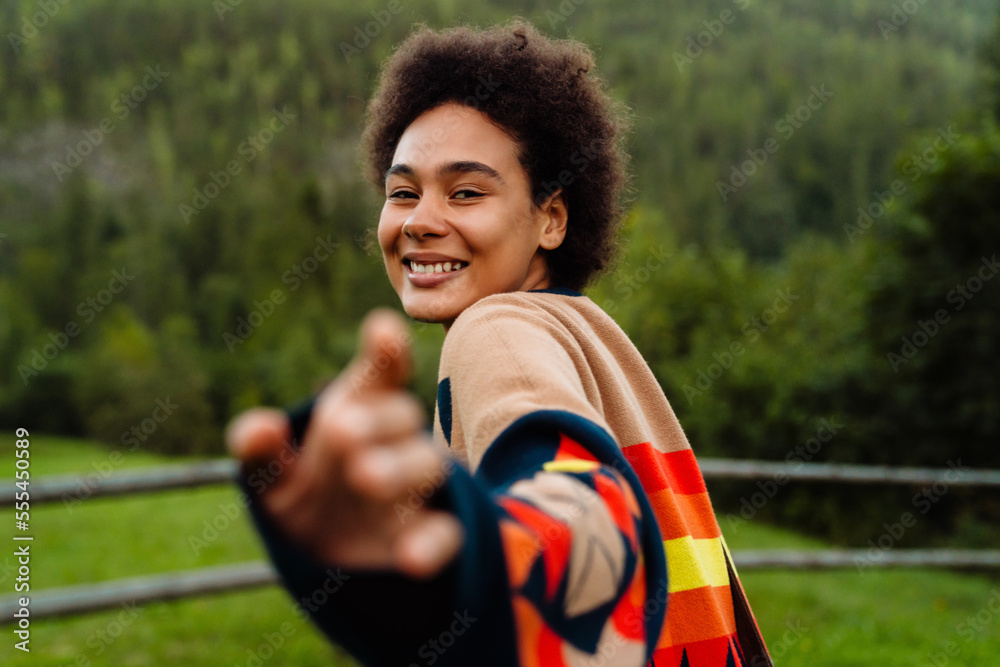 Εκτύπωση καμβά Smiling young african woman stretching her hand to the camera while standing in