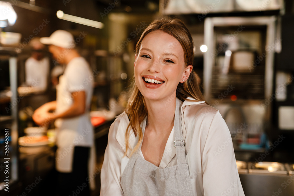 Beautiful woman chef cook smiling at camera while standing in kitchen of a restaurant