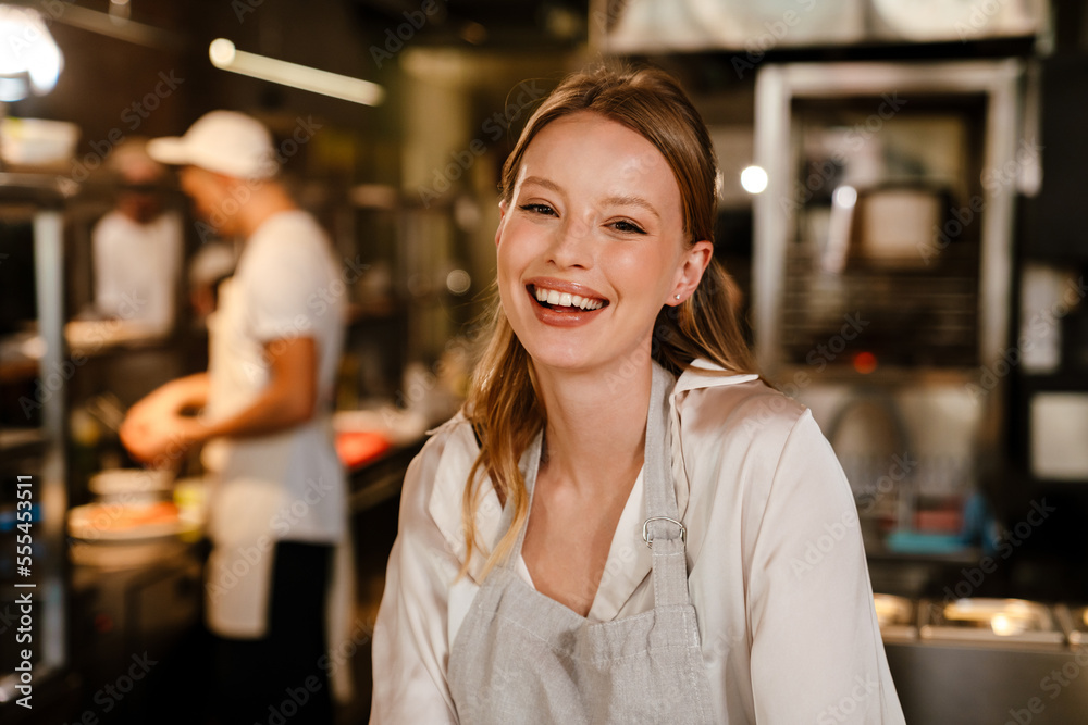 Beautiful woman chef cook smiling at camera while standing in kitchen of a restaurant