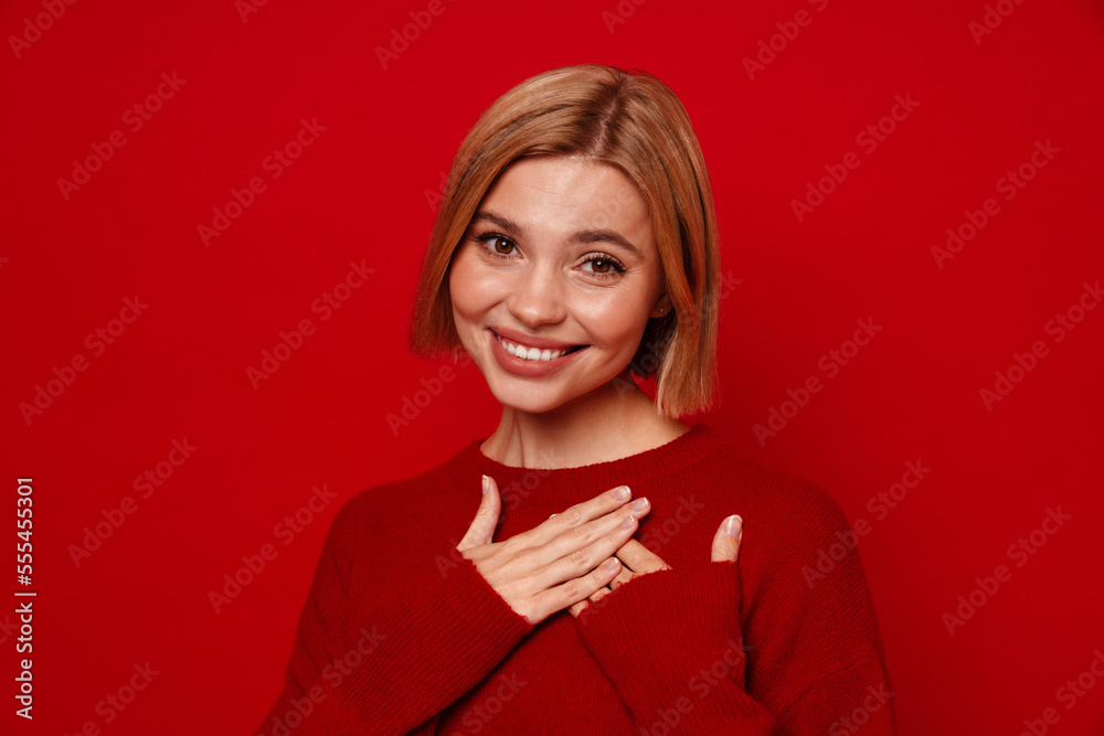 Lovely woman smiling and holding her hands on chest isolated over red background Lovely woman smiling and holding her hands on chest isolated over red background