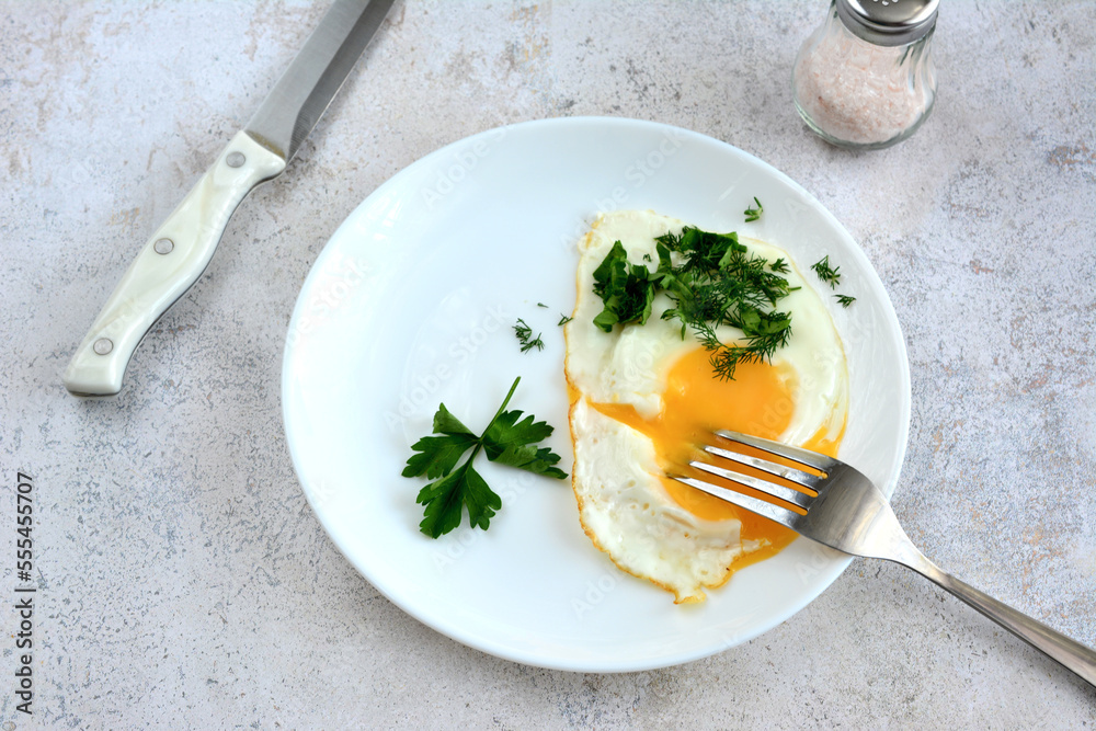 fried egg with yellow yolk on plate with fork and knife, view from top