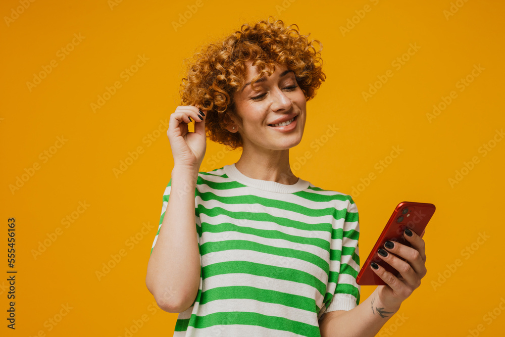 Curly ginger woman in striped t-shirt smiling and using mobile phone Curly ginger woman in striped t-shirt smiling and using mobile phone