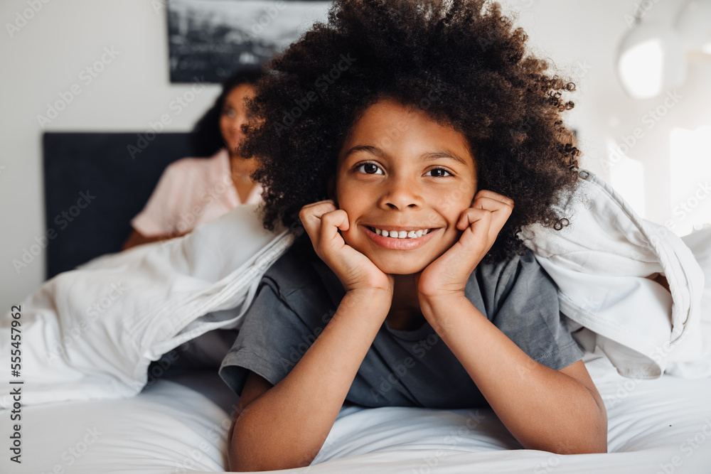 Happy black little boy smiling while lying in bed with his family Happy black little boy smiling while lying in bed with his family