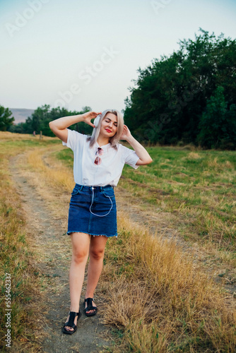 A sweet, young, happy, cheerful, pretty woman, walking outdoors in the park on a beautiful summer day. The girl listens to music with headphones.