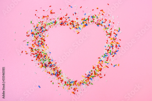 Bunte Zuckerstreusel in Kontur eines Herzens auf einem rosa Hintergrund von oben