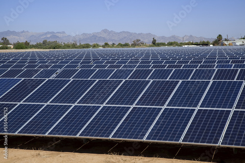 Close-up of solar panels with farm buildings and mountains beyond, near Blythe; California, United States of America